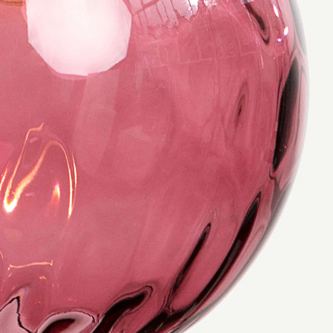Gros plan sur la texture ondulée du verre strié rose fuchsia d'un globe Trilogie.